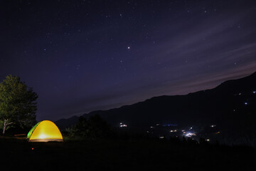 Fototapeta na wymiar Beautiful view of mountain landscape with glowing yellow camping tent at night