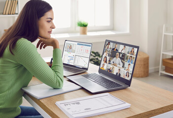 Team of colleagues who are working from home in lockdown create online network, meet and discuss their agenda. Young woman sitting at desk and looking at laptop screen during sales report presentation
