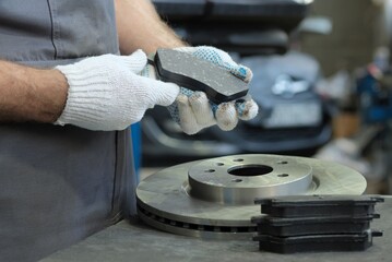 Spare parts for a passenger car. An auto mechanic inspects the brake pads. There is a brake disc...