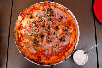 pizza with bacon, mushrooms, tomatoes and cheese lies in a white plate with sauce on a wooden table. Italian cuisine. kind of super