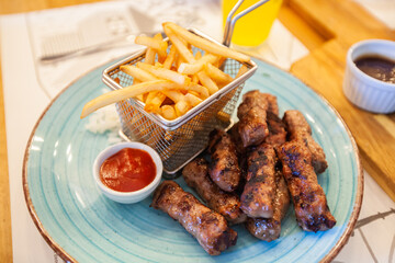 Traditional grilled meat kebab with french fries serving on restaurant table.