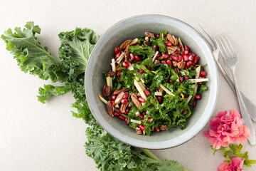 a bowl of kale, pomegranate, apple and pecan salad on a light table, space for text