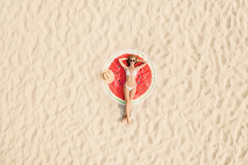 Woman sunbathing on round beach towel at sandy coast, aerial view