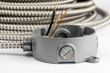 a loose coil of armored electrical cable with stripped conductors and a cast metal octagon junction...