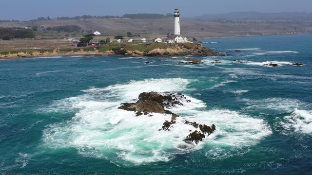 Pacific Ocean waves crash against the scenic coastline of California near Santa Cruz. A beautiful lighthouse stands on the edge of the sea providing visual warning for passing ships.