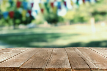 Empty wooden table in park decorated with bunting flags, space for design. Outdoor party