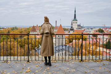 Blonde woman enjoy panorama of the city of Tallinn. Amazing scenic view of the old town. Girl explore Estonia, Europe. City and sea. City autumn landscape, old historical architecture. - obrazy, fototapety, plakaty