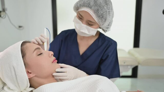 Beautiful Asian woman lying on bed and professional cosmetologist making mesotherapy derma pen procedure to face augmentation for anti-wrinkle in beauty clinic. Treatment and rejuvenation face concept