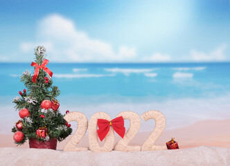Merry Christmas. New Year concept. Christmas tree on a hot beach and the inscription 2022 on sand