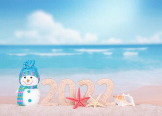 Fototapeta premium New year 2022 sign with snowman on beach background