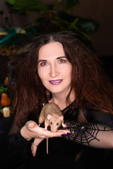Portrait of a witch in black clothes with disheveled hair with a rat in her hands. Halloween celebration concept.