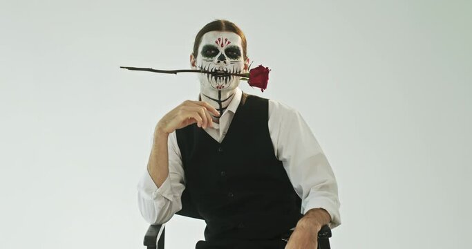 Man with creepy makeup biting red rose