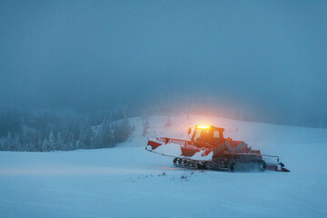 Ratrak in action on the morning ski slope. Machine for skiing slope preparations with headlights on in snowy mountains