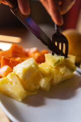 Hands cutting sliced fruit with fork and knife on plate
