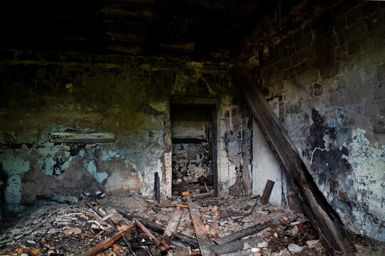 An abandoned building to be demolished, with sooty walls and a collapsed plank ceiling, after a fire.