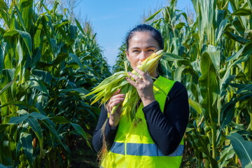 Female agronomist farmer examining and smelling unripe green corn maize