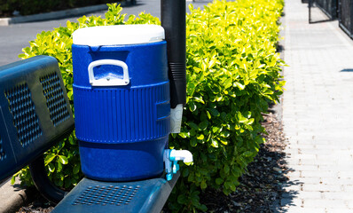 Blue water jug with cups and a cup dispenser on a blue bench