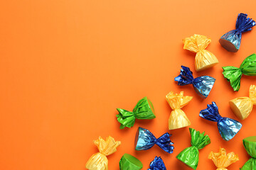 Many candies in colorful wrappers on orange background, flat lay. Space for text