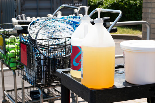 Two large bottles of hand sanitizer on a table next to tennis rackets and balls
