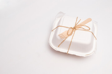 Packed bento cake in white eco-friendly packaging, tied with jute and a wooden fork. White background with space for text. Selective focus.