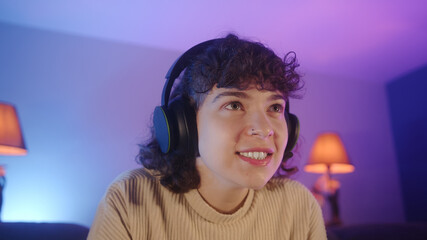 Portrait of excited cute gamer girl with curly-haired. Young girl sitting and playing a video game with headset