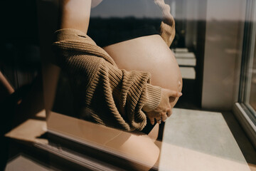 Closeup of a pregnant woman standing by the window in sunlight.