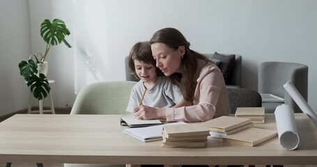 Cheerful young mother assisting her adorable son with schoolwork and exercises. Difficulties with school preparation and learning to write and draw. Happiness and support in the family