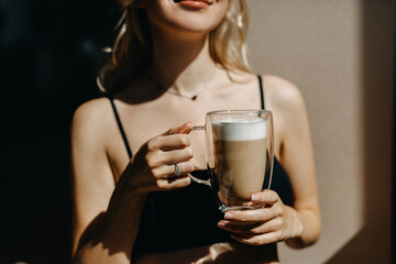 Closeup of a woman drinking coffee from a double glass cup, in sunlight.