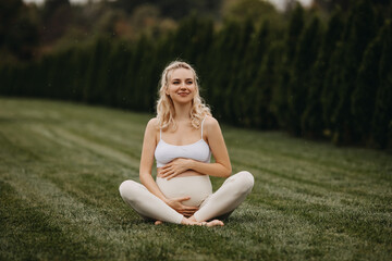 Fototapeta na wymiar Pregnant woman sitting on green grass outdoors, in a park, smiling.