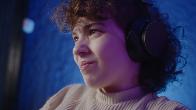 Beautiful curly-haired young e-sportsgirl or gamer playing try-hard game. She wearing headphones play video games