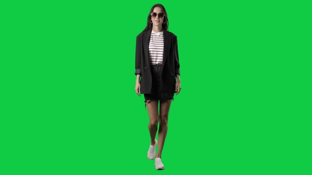 Happy springtime style woman with sunglasses in blazer walking. Full body on green screen chroma key background