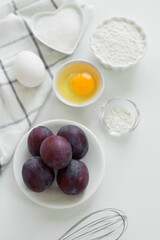 Step by step recipe for baking sweet plum pie. Ingredients set for cooking. Flour, eggs, sugar, plums for sweet pastries on white background. Culinary light background