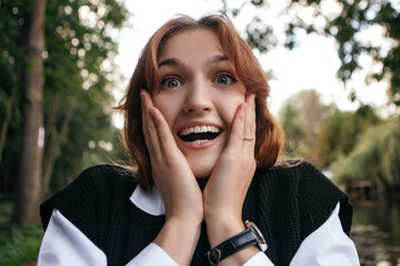 Surprised shocked happy woman smiling screaming yellingoutside holding head euphoria gesturing...
