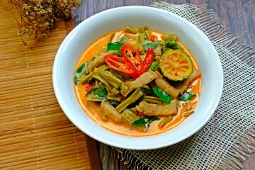Authentic Thai red curry with pork belly and morning glory (Gaeng Tay Po) on wooden table. Thai food.