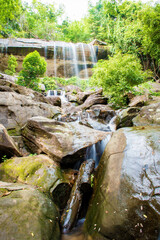 A small waterfall falls from a cliff flowing through a large rock.