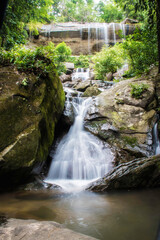 A small waterfall falls from a cliff and flows through a large rock with turbulent water.