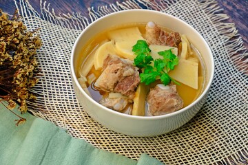 Fresh sweet bamboo shoot boiled with pork bones soup in white bowl on wooden table. Thai food.
