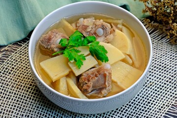 Fresh sweet bamboo shoot boiled with pork bones soup in white bowl on wooden table. Thai food.