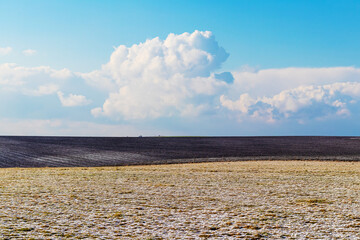 The field with dry grass and plowed land is covered with the first snow. Picturesque clouds over...
