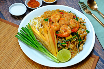 Fried rice noodle with shrimp (Pad Thai Goong Sod) in white plate with sugar, peanut and chili plate on wooden table.