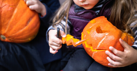 Little girls make jack-o-lantern from big pumpkins for celebratiion of halloween holiday.Witch costume, hat, coat. Cut with knife,take out pulp with seeds.Outdoors activity, backyard.Children's party