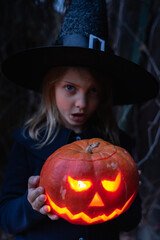 Girl in witch costume, hat with jack-o-lantern.Hand made from big pumpkin. Candle lights in eyes,nose,mouth. Celebratiion of halloween holiday.Cut by knife.Outdoors activity,backyard.Children's party