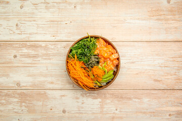Top view image of salmon poke bowl with white rice, wakame salad, masago roe, guacamole slices and sesame seeds