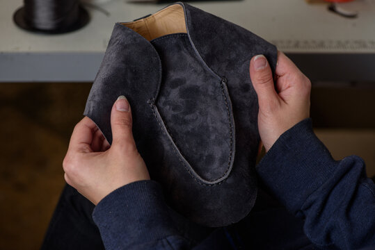 Shoemaker checking quality of the seam of handmade shoes in workshop. Female hands holding craft leather shoe.