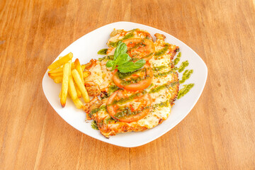 Veal schnitzel with melted mozzarella cheese, pesto sauce, basil, tomato slices and a side of French fries
