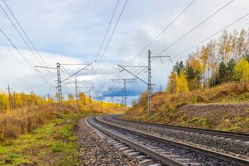 Fototapeta na wymiar Golden autumn landscape on empty curved railroad in Siberia. Industrial landscape. Railroad tracks turn right. Electric poles with wires along the railway