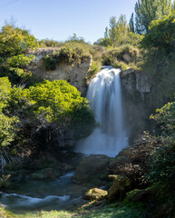 Beautiful autumn scene where a huge waterfall of water falls into the void of a canyon on a sunny autumn day, creating a relaxing atmosphere. Long exposure photography concept, autumn landscape.