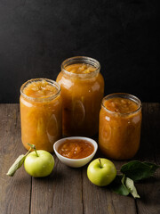 Tasty homemade apple jam, confiture in a glass jar with apples on a black wooden table
