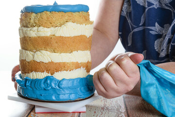 High key photo. Baker using a icing nozzle to put blue frosting on the base of the cake.