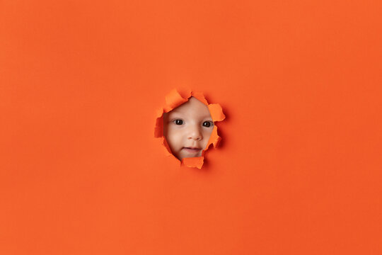 Young baby peeking through orange paper